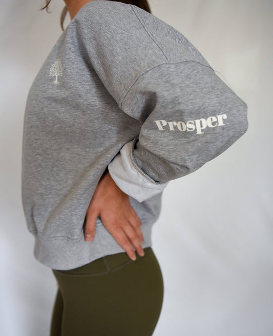 Cotton Dream Sweatshirt in Grey from side view with "Prosper" on sleeve and sleeve rolled up for casual look, paired with Olive Anthem Leggings